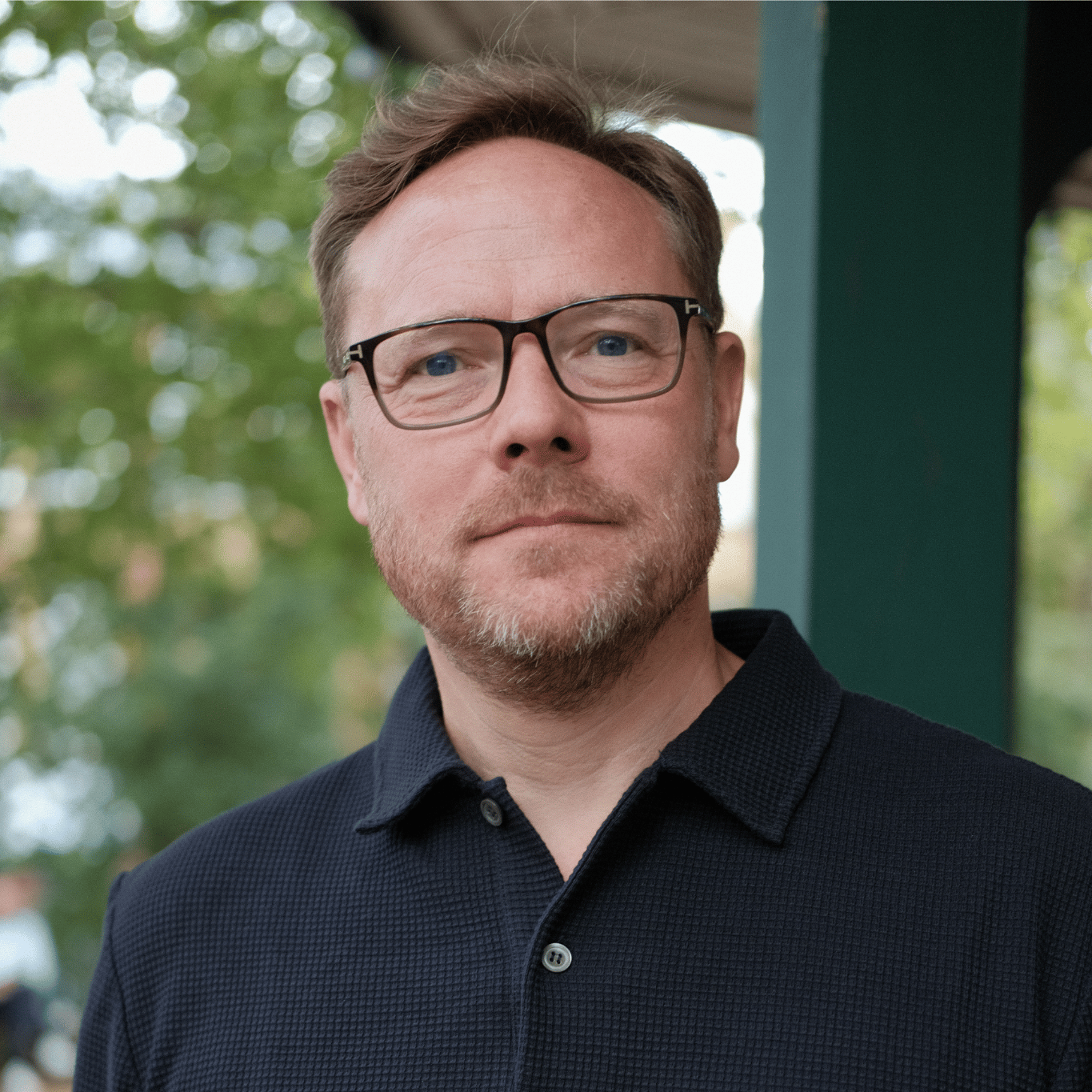 Portrait of Andy Goldsmith, wearing glasses and a navy blue polo shirt. He is smiling.