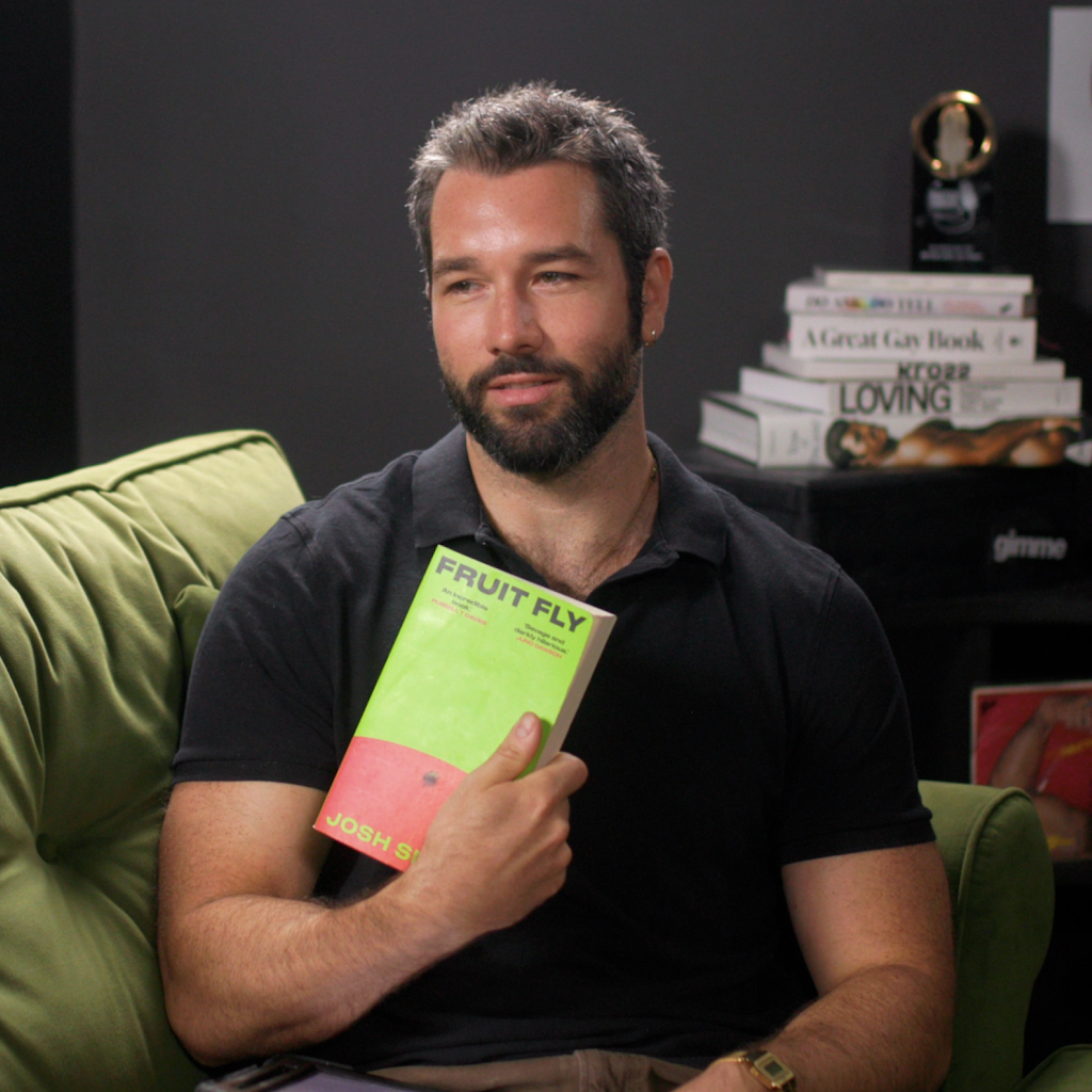Photo of Jon Dean sat on a sofa holding a book to his chest.